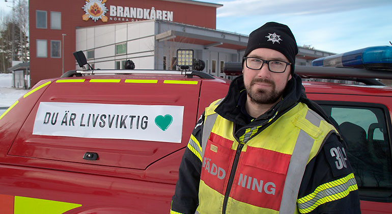 En brandman står framför en mindre brandbil som har dekalen "Du är livsviktig" följt av ett grönt hjärta.