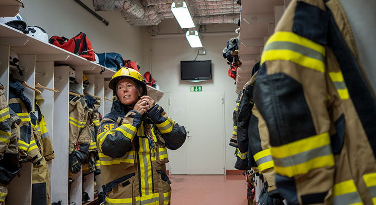 En kvinnlig brandman knäpper sin hjälm i ett omklädningsrum.