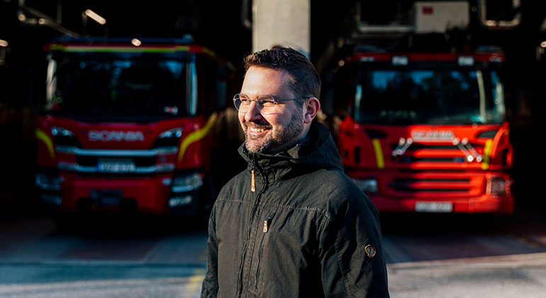 Brandingenjören och doktoranden Mateusz Sosnowski står framför ett garage med två brandbilar.