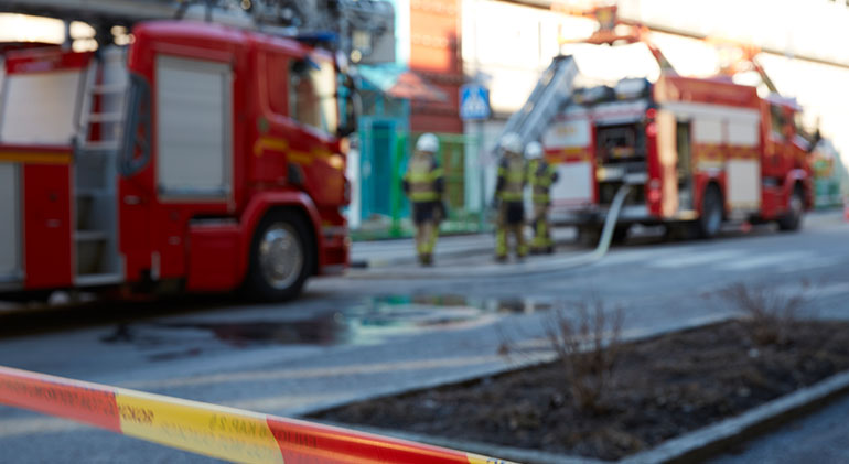 Ett avspärrningsband med brandbilar och brandmän bakom.
